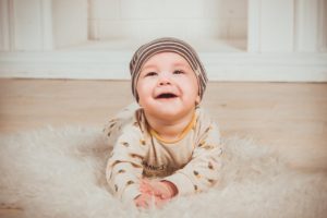 A happy, smiling baby laying on their tummy on a white fluffy rug.