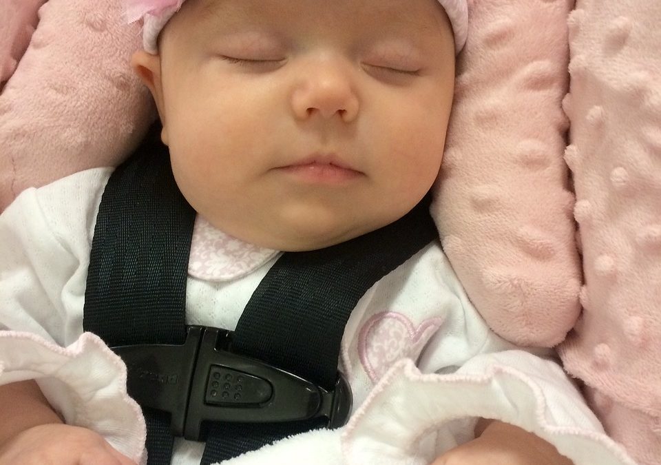 A blissfully sleeping baby comfortable and secure in a plush pink safety car seat.